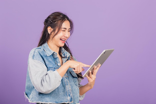 Porträt einer asiatischen schönen jungen Frau, die mit einem Tablet-Computer lächelt, glücklicher weiblicher Teenager-Touchscreen auf einem digitalen Tablet-PC, Studioaufnahme isoliert auf violettem Hintergrund