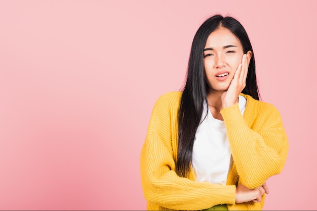 Porträt einer asiatischen schönen jungen Frau, die unter Zahnschmerzen leidet, weibliche schreckliche Schmerzen bei starken Zähnen, die die Hand ans Kinn drücken, Studioaufnahme isoliert auf rosa Hintergrund, Konzept der Zahngesundheit