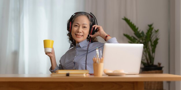 Porträt einer asiatischen Senior Business-Frau mit Kopfhörern und Kaffee mit Videoanruf am Morgen zu Hause Konto- und Finanzkonzept