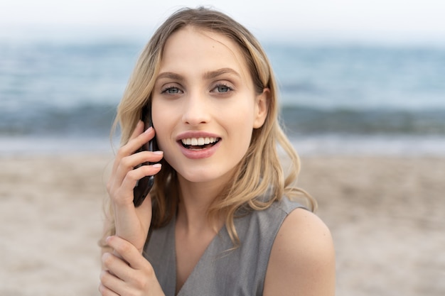 Porträt einer atemberaubenden blonden Frau, die auf dem Handy mit einem niedlichen Lächeln spricht, das in die Kamera schaut