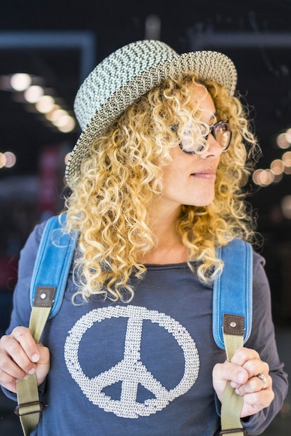 Foto porträt einer attraktiven jungen erwachsenen frau auf reisen mit rucksack in der flughafengate-station konzept des reisenden weibliche menschen und unabhängigkeit blonde lockige dame genießen urlaubsreise und lächeln suchen