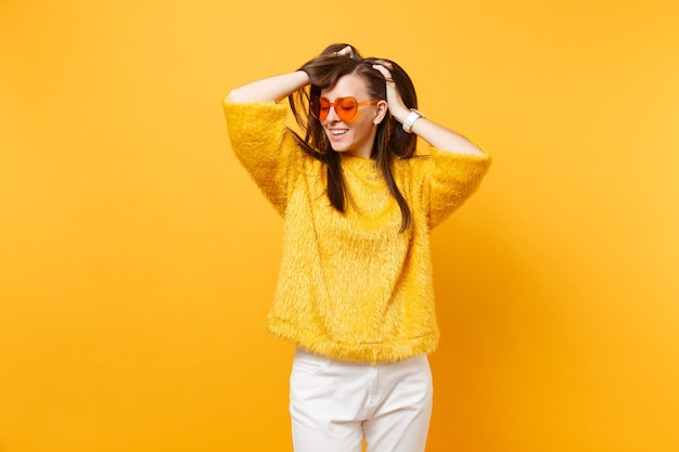 Porträt einer attraktiven jungen Frau im Pelzpullover, weiße Hosenherz-Orange-Brille, die sich am Kopf festklammert, isoliert auf hellgelbem Hintergrund. Menschen aufrichtige Emotionen, Lifestyle-Konzept. Werbefläche.