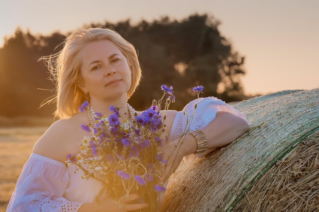 Porträt einer attraktiven jungen Frau im Retro-Kleid mit einem Strauß Wildblumen auf dem Land