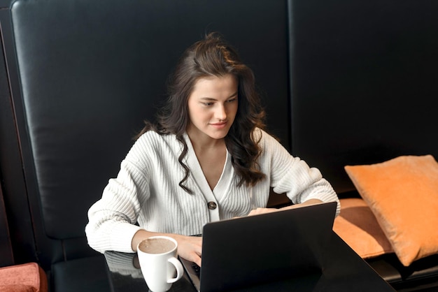 Porträt einer attraktiven jungen kaukasischen Frau, die einen Laptop in einem Café verwendet Junge weibliche Freiberufler, die an einem Laptop-Computer in einem Café arbeiten