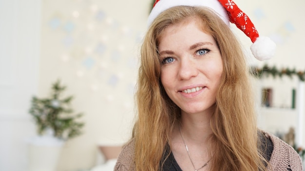 Porträt einer attraktiven lächelnden Frau in Weihnachtsmütze zu nome - helles gemütliches Zimmer