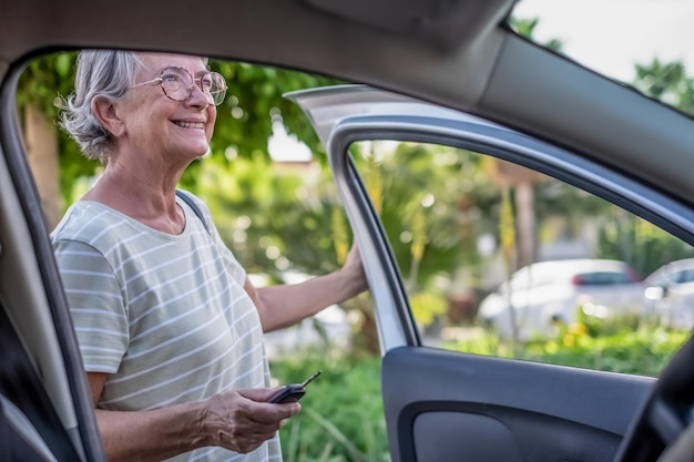 Porträt einer attraktiven Seniorin im T-Shirt, die ihr Auto betritt Mit einer Hand hält die Frau die Schlüssel und mit der anderen die Tür