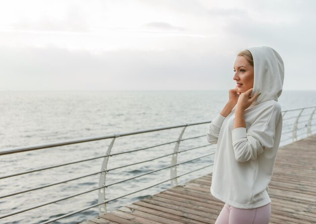 Porträt einer attraktiven, süßen Sportlerin im weißen Hoodie am Strand