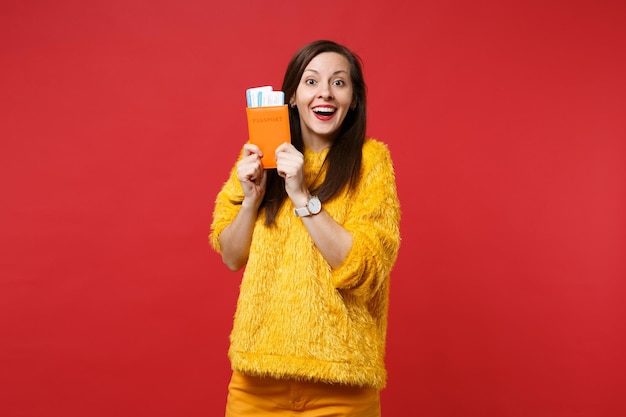 Porträt einer aufgeregten Frau im gelben Pelzpullover mit Reisepass, Bordkarte einzeln auf hellrotem Wandhintergrund im Studio. Menschen aufrichtige Emotionen, Lifestyle-Konzept. Kopieren Sie Platz.
