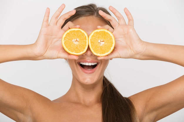 Foto porträt einer aufgeregten jungen topless frau isoliert, die geschnittene orange an ihrem gesicht hält