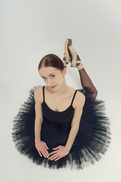 Porträt einer Ballerina in einem schwarzen Tutu, die auf dem Boden liegt und sich auf ihre Hände stützt