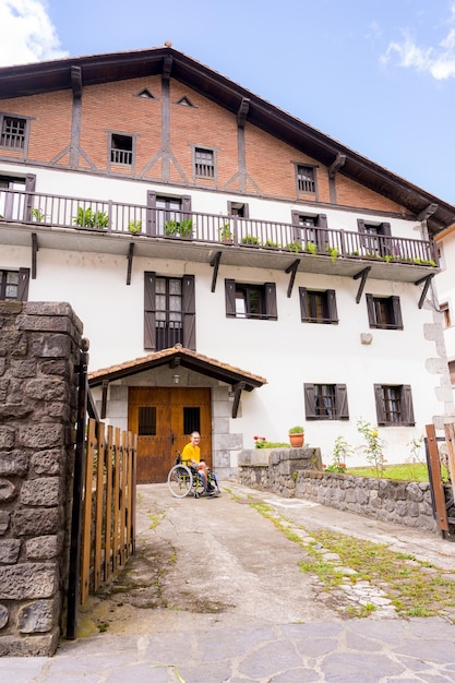 Porträt einer behinderten Person im Rollstuhl neben einem schönen Landhaus