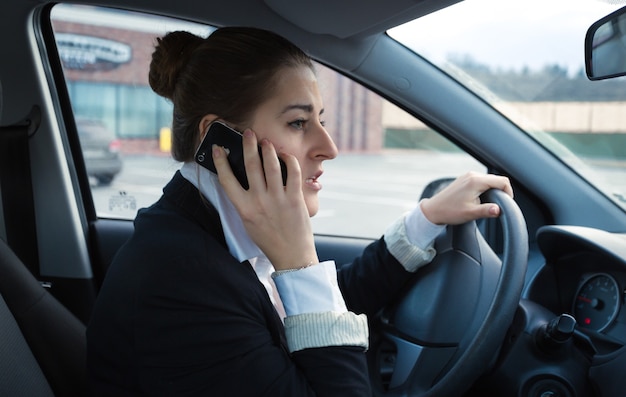 Porträt einer besorgten Geschäftsfrau, die Auto fährt und telefoniert