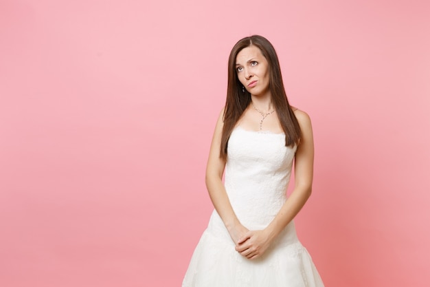 Porträt einer besorgten verärgerten Frau im weißen Kleid, die Händchen haltend vor ihr gekreuzt steht