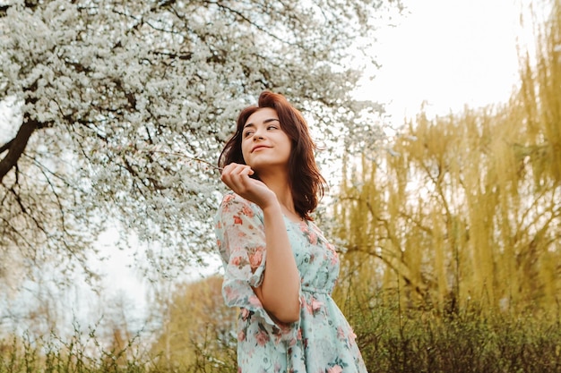 Porträt einer bezaubernden Frau, die in der Nähe von blühenden Blumen des Apfelkirschbaums im Garten posiert