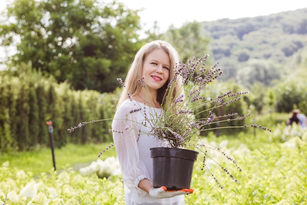 Porträt einer blonden Frau, die Blumentopf mit Lavendel im Greenshop hält