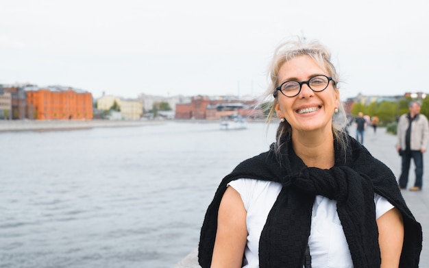 Foto porträt einer blonden frau mit brille und einem schwarzen pullover, der im freien über ihre schultern gebunden ist