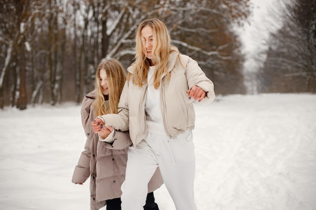 Porträt einer blonden Mutter und jugendlich Tochter, die im Winterwald laufen