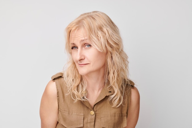 Foto porträt einer blonden, reifen frau, die isoliert auf weißem studiohintergrund misstrauisch in die kamera blickt und ungläubig blinzelt