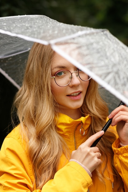 Porträt einer Blondine in einem gelben Regenmantel mit einem Regenschirm in der Nähe