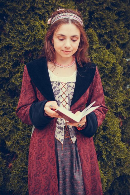 Porträt einer brünetten Frau in historischer barocker Kleidung, die im Freien ein Buch liest