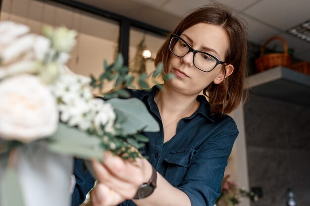 Porträt einer brünetten Frau mit Brille über Blumenstrauß gebeugt, Floristenarbeit konzentriert.