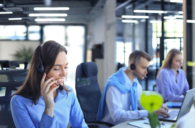 Porträt einer Call-Center-Mitarbeiterin, die von ihrem Team begleitet wird Lächelnder Kundendienstmitarbeiter bei der Arbeit