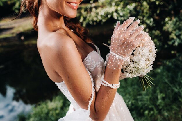 Porträt einer eleganten Braut in einem weißen Kleid mit einem Blumenstrauß in der Natur in einem Naturpark. Modell in einem Hochzeitskleid und Handschuhen und mit einem Blumenstrauß. Belarus.