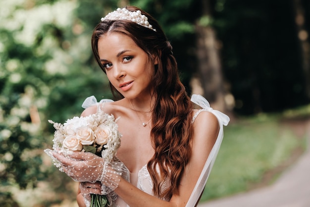 Porträt einer eleganten Braut in einem weißen Kleid mit einem Blumenstrauß in der Natur in einem Naturpark.