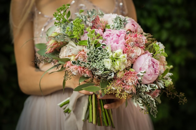 Porträt einer eleganten unerkennbaren hübschen Frau, die graues Hochzeitskleid trägt und in der Straße aufwirft. Die Braut hält einen Strauß Pastellblumen und viel Grün