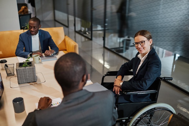 Porträt einer erfolgreichen Geschäftsfrau, die bei Meetings einen Rollstuhl benutzt und mit einer Gruppe von Kollegen in modernen Büroräumen spricht