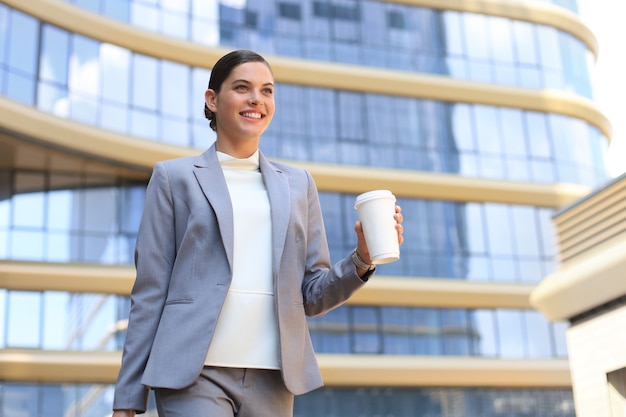 Porträt einer erfolgreichen Geschäftsfrau, die mit Kaffee in der Nähe des Bürogebäudes auf der Stadtstraße zur Arbeit geht.