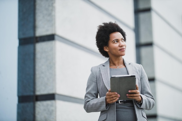 Porträt einer erfolgreichen schwarzen Geschäftsfrau, die während einer kurzen Pause vor einem Firmengebäude ein digitales Tablet verwendet.
