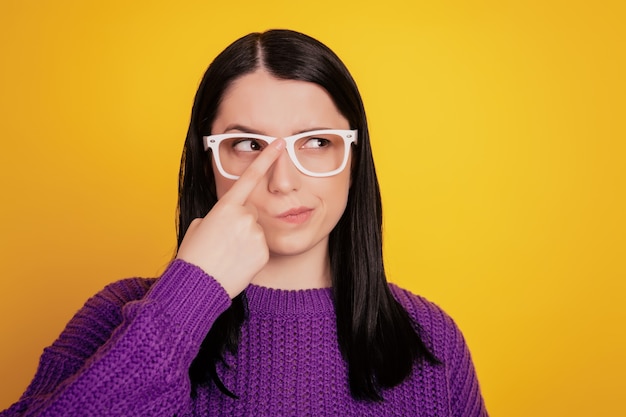 Porträt einer ernsten Handberührungsbrille des jungen Mädchens, die korrektes, selbstbewusstes Denken fixiert, sieht leer aus, isoliert auf gelbem Hintergrund