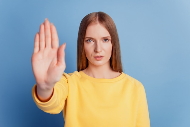 Porträt einer ernsthaften attraktiven Dame, die Handshow-Stop-Geste auf blauem Hintergrund anhebt