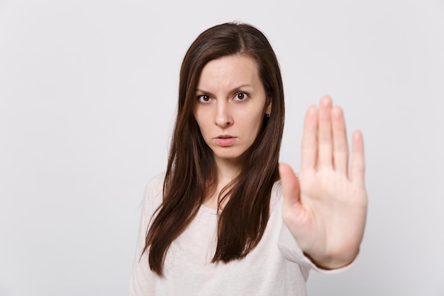 Porträt einer ernsthaften besorgten jungen Frau in leichter Kleidung, die eine Stopp-Geste mit der Handfläche zeigt, die auf weißem Wandhintergrund im Studio isoliert ist. Menschen aufrichtige Emotionen, Lifestyle-Konzept. Kopieren Sie Platz.