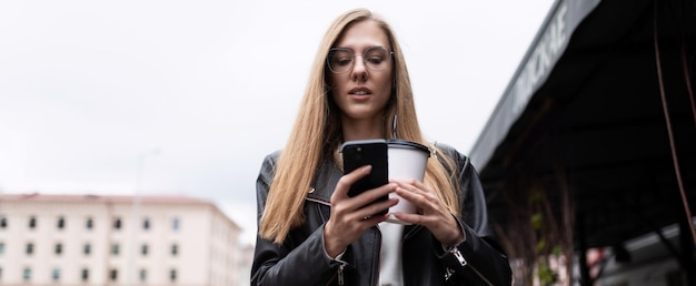 Porträt einer ernsthaften jungen Frau mit einer Tasse Kaffee, die auf ein Mobiltelefon blickt