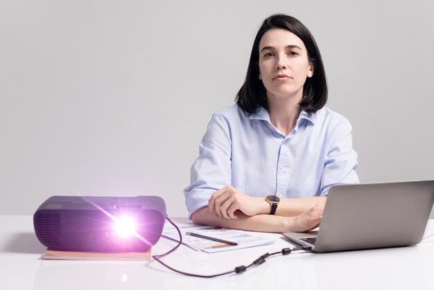 Porträt einer ernsthaften selbstbewussten weiblichen Führungskraft, die mit Laptop und Papieren am Tisch sitzt und Präsentation beim Treffen beobachtet