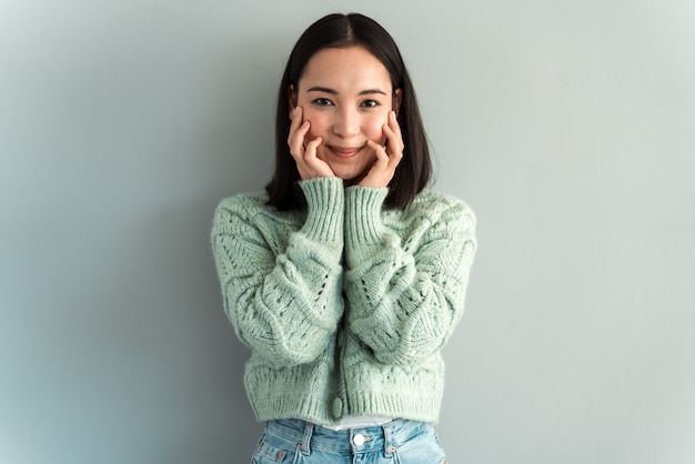 Porträt einer erstaunten süßen Frau, die Gesicht mit den Händen hält und mit Freude in die Kamera schaut. Indoor-Studioaufnahme auf grauem Hintergrund isoliert