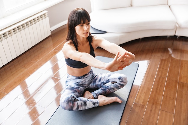 Porträt einer erwachsenen Frau, die ihren Körper beim Sport oder Yoga auf der Matte in einem hellen Raum zu Hause streckt