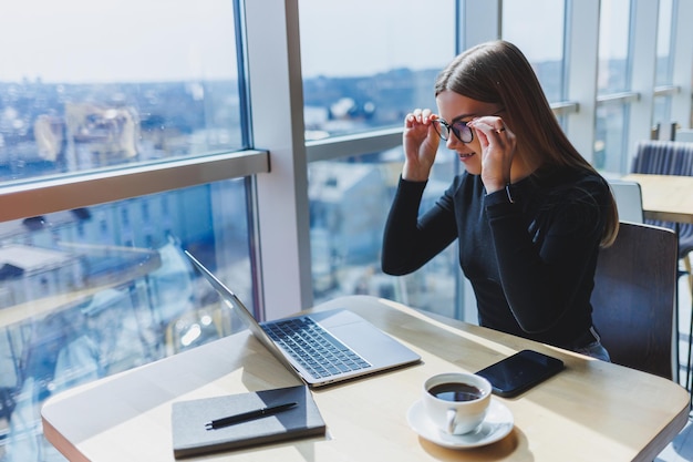 Porträt einer europäischen jungen und erfolgreichen Frau, die in einem modernen Café mit Laptops sitzt Hübsche Freiberuflerin genießt ihre Freizeit in einem Café