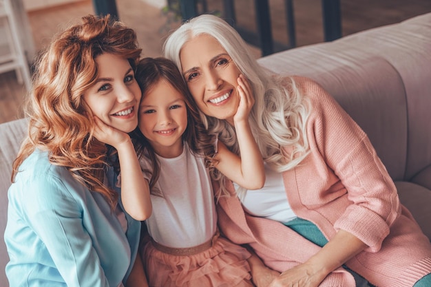 Porträt einer Familie aus drei Generationen, die auf dem Sofa sitzt und in die Kamera schaut