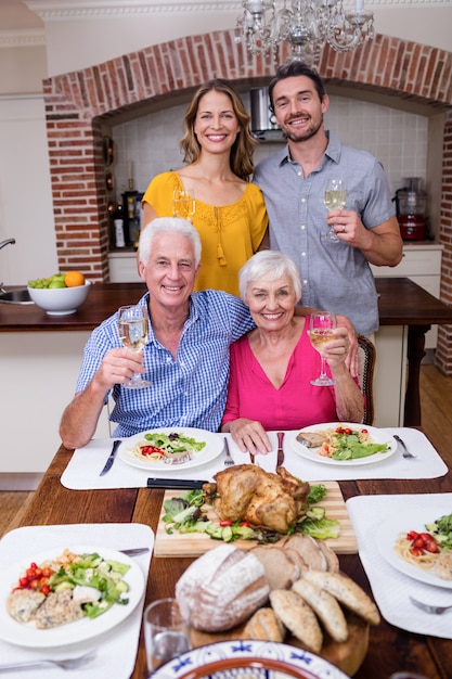 Porträt einer Familie mit zwei Generationen, die bei Tisch ein Weinglas hält