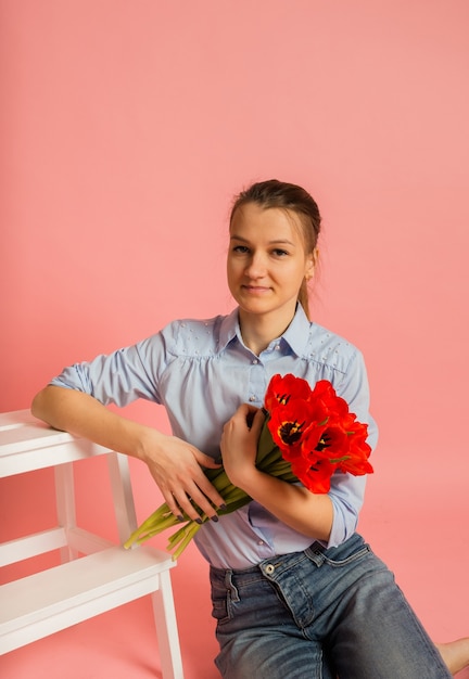 Porträt einer Frau, die auf dem Boden sitzt und einen Strauß Tulpen an einer rosa Wand mit einer Kopie des Raumes hält