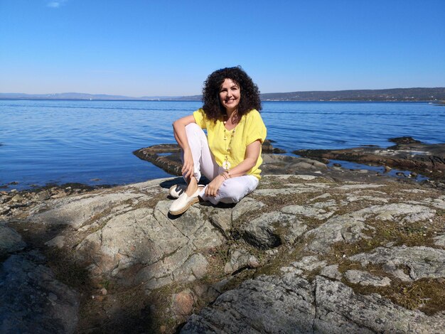 Foto porträt einer frau, die auf einem felsen gegen das meer sitzt