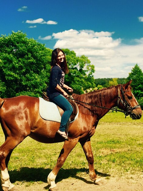 Foto porträt einer frau, die auf einem pferd auf dem feld gegen den himmel reitet