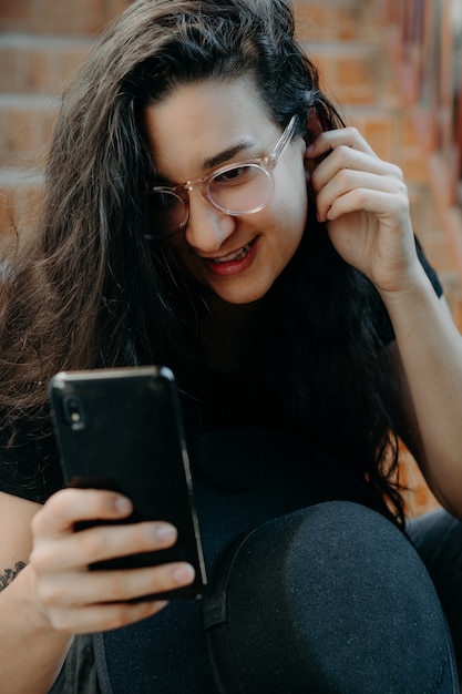 Porträt einer Frau, die das Handy benutzt und eine Brille und einen schwarzen Hut trägt.