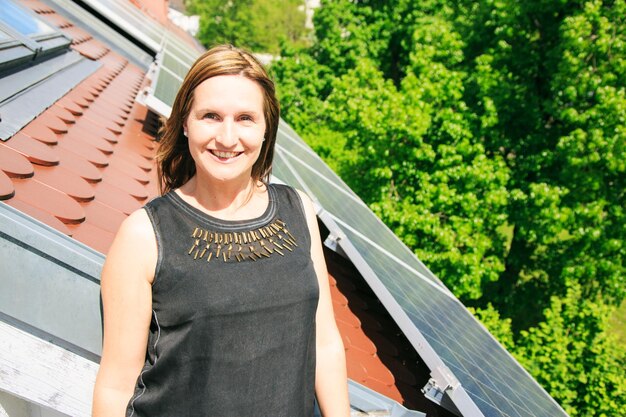 Foto porträt einer frau, die durch ein fenster durch sonnenkollektoren auf dem dach pflückt