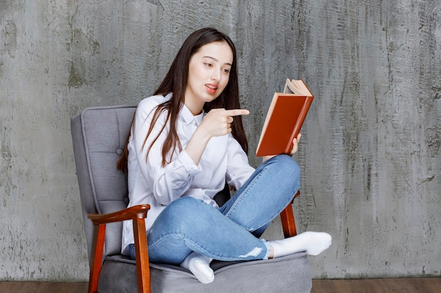 Porträt einer Frau, die ein Buch liest, während sie auf einem Sessel sitzt. Foto in hoher Qualität