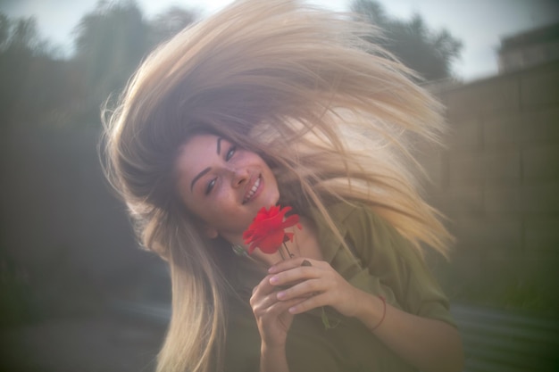 Foto porträt einer frau, die eine rote rose gegen den himmel hält