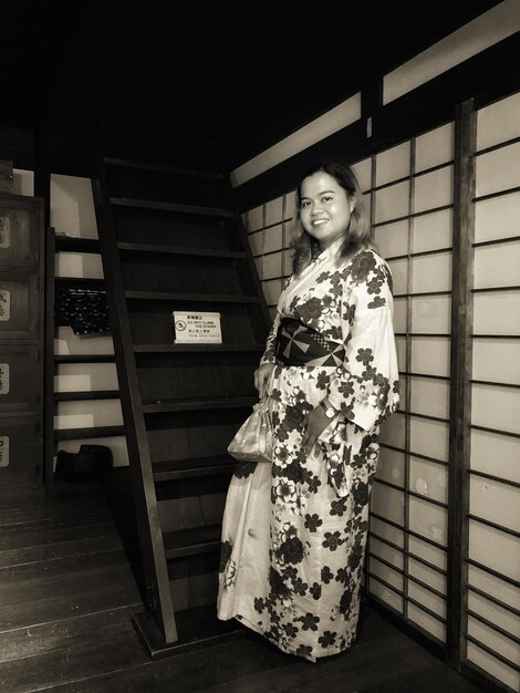 Foto porträt einer frau, die einen kimono trägt, während sie zu hause gegen eine leiter steht